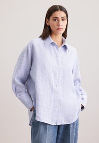 Camicia a righe blu chiaro e bianca, con colletto e vestibilità rilassata. Presenta maniche lunghe e dettagli con bottoni in evidenza.