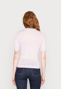 Suéter curto de manga curta em rosa claro, com um design justo, apresentando um decote redondo e uma textura suave, combinado com jeans escuros.
