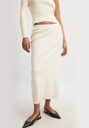 Cream ribbed knit two-piece set featuring a fitted long-sleeve top and a matching ankle-length skirt; sleek black pointed flats complete the look.