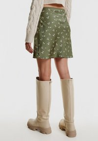 Vihreä mini-hame, jossa on kukkakuosi ja sileä tekstuuri, yhdistettynä korkeisiin beigeihin kumikenkäbootseihin, joissa on paksut pohjat ja tyylikäs muotoilu.