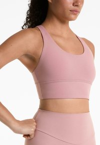Roze sportbeha met een gladde textuur, brede schouderbanden en een strakke pasvorm, met een horizontale naad over de band.