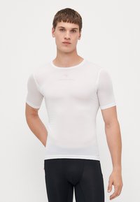 T-shirt de sport blanc à manches courtes avec une coupe ajustée, fabriqué en tissu texturé et respirant. Dispose d'un logo sur la poitrine.