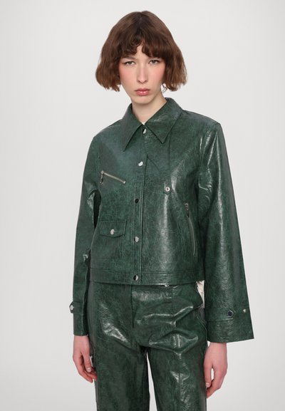 Giacca in ecopelle verde con un design corto, ampio colletto, tasca frontale con zip e bottoni in metallo argentato. La texture è lucida con una finitura stropicciata.