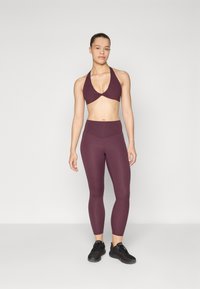 Reggiseno sportivo bordeaux con design a halter, abbinato a leggings a vita alta bordeaux. Tessuto liscio e materiale elasticizzato. Scarpe da ginnastica nere.