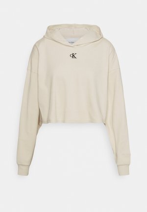 Kremowa krótka bluza z kapturem z długimi rękawami i małym czarnym logo "cK" na środku klatki piersiowej.
