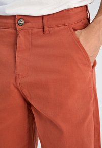 Katoenen broek in roestkleur met een rechte pijp, uitgevoerd met een knoopsluiting, zijzakken en een gladde textuur.