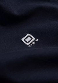 Tummansininen kangaspaita, jossa on valkoinen "ombre"-logo neliön muotoisena, sileä rakenne vähäisellä venymisellä, sijoitettu keskeisesti vaatteeseen.