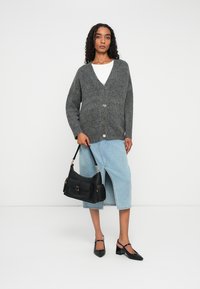 Grå strikket cardigan med v-hals, med store knapper. Kombinert med et lys blått denimskjørt og en svart håndveske. Svart hæler fullfører antrekket.