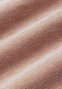 Teksturowana tkanina w odcieniach jasnobrązowym i kremowym, z plecionym wzorem o delikatnej strukturze siatki. Miła i gładka w dotyku.