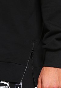 Felpa nera con cerniera laterale e orlo a costine. Il tessuto sembra morbido e uniforme, senza motivi o loghi visibili.