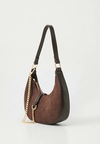 Sac à épaule en daim marron de forme arrondie, avec un accent en chaîne dorée, une fermeture éclair latérale et une sangle en cuir foncé. Détail de surface texturée.