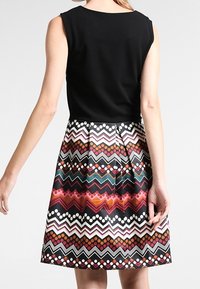 Ärmlös svart topp som övergår till en flerfärgad mönstrad kjol med zigzag- och prickmönster i röda, vita och gröna nyanser.