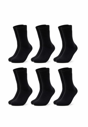 Person wearing black crew socks over beige ribbed tights, standing with feet slightly apart on a white surface.