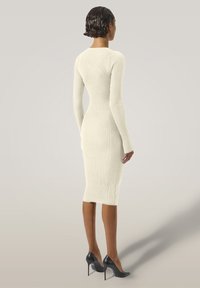 Abito midi a maglia a coste in bianco avorio, con maniche lunghe e silhouette aderente. Indossato con tacchi alti neri; texture liscia e forma strutturata.