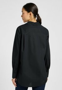 Zwarte lange mouwen shirt met een traditionele kraag, gemaakt van soepel stof, met knoopmanchetten en een rechte achterkant.
