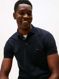 Marineblå polo skjorte med teksturert stoff, to knapper og en liten rød, hvit og blå logo på venstre bryst. Korte ermer, vanlig passform.