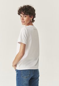 Camiseta blanca de manga corta, con cuello redondo, combinada con jeans de mezclilla azul. Textura suave, corte relajado, con costuras y costuras visibles.