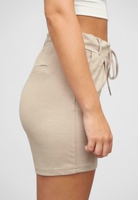 Shorts aderenti beige realizzati in tessuto morbido, con vita regolabile tramite cordoncino e tasche laterali. Texture liscia con un design pulito e semplice.