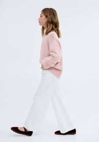 Ljusrosa stickad tröja, vita vida byxor och burgundy tofflor, visade på en person som går från vänster till höger.