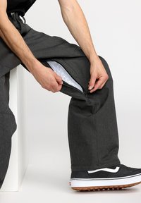 Szare materiałowe spodnie z zamkiem błyskawicznym, odsłaniające białą siateczkową podszewkę. Noszone z czarnymi trampkami z białymi akcentami i podeszwą z gumy.