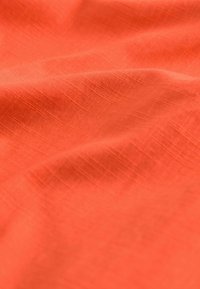 Tekstylia w żywej koralowej barwie o miękkiej, gładkiej teksturze i delikatnym wzorze tkanym, ukazujące łagodne fałdy i zagięcia.