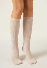 Beige kniehohe Socken mit einer gerippten Textur und elastischem Abschluss, aus einem weichen Strickmaterial, geeignet für den täglichen Gebrauch.