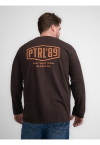 Brown overhemd met lange mouwen van katoen, voorzien van een groot oranje geprint ontwerp op de achterkant met de teksten "PTRL'89" en "ALASKA'89".
