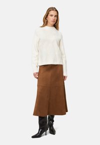 Pull blanc duveteux avec un motif en forme de losange, jupe mi-longue en daim marron, et bottes noires à talons aiguilles jusqu'aux genoux. Boucles d'oreilles simples en accent.