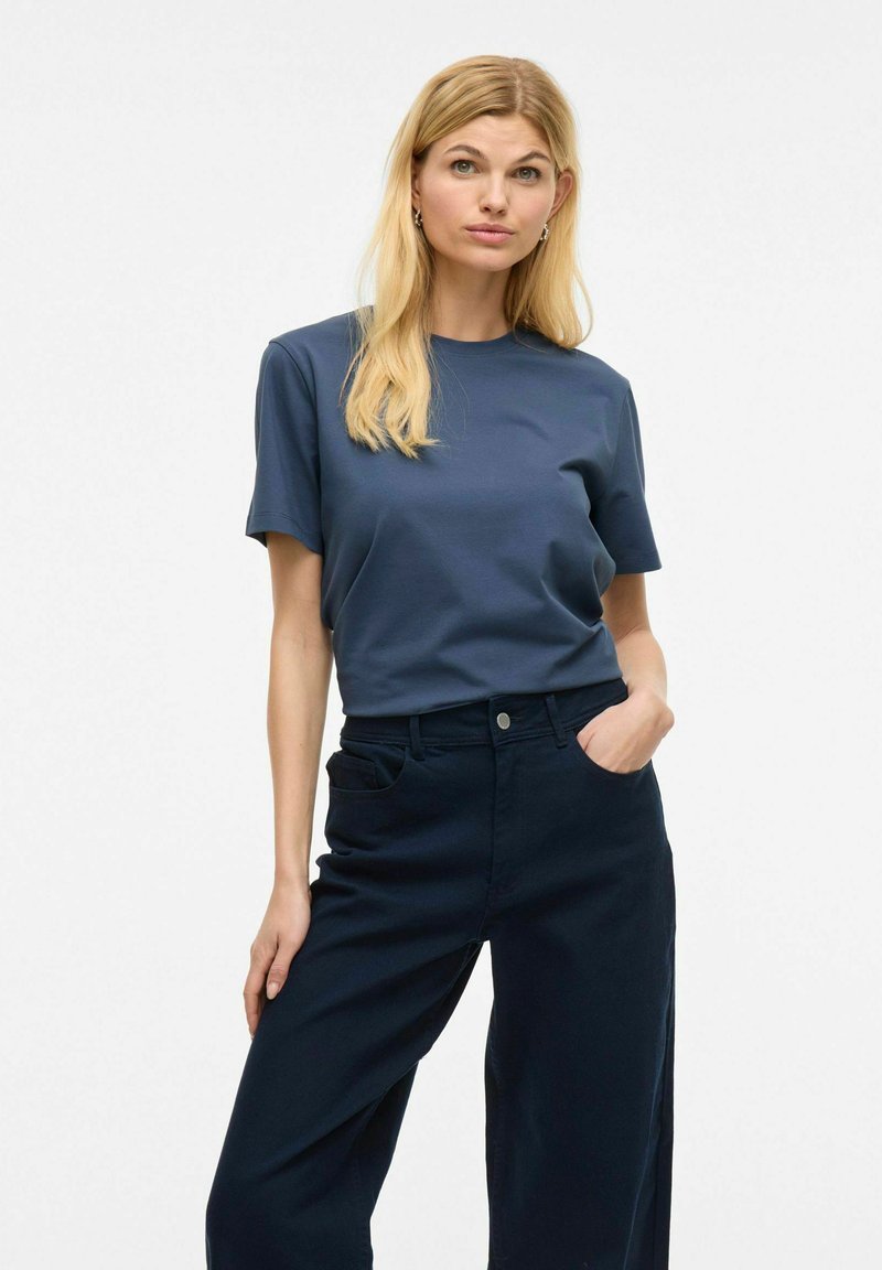 Camiseta de cuello redondo azul marino, de manga corta, hecha de una tela suave, combinada con pantalones anchos azul marino que cuentan con bolsillos laterales y un cierre de botón.