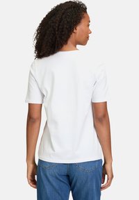 T-shirt en coton blanc avec un col rond et des manches courtes. L'arrière présente une surface lisse et dépouillée avec une coupe décontractée. Associé à un jean en denim bleu.
