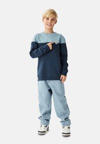 Merensininen ja vaaleansininen collegepaita, jossa pitkät hihat ja resorit hihoissa, yhdistetty vaaleansinisillä löysillä farkuilla ja mustavalkoisilla tennareilla.