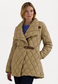 Casaco bege acolchoado com um colarinho largo, fecho de pressão e detalhes em couro. Apresenta um ajuste solto e um padrão de costura diagonal.