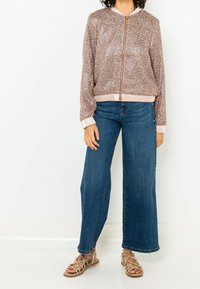 Floral-patterned bomber jacket with a gold zipper, paired with wide-leg blue jeans and strappy flat sandals, showcasing a relaxed fit.