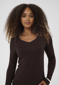 Brun langærmet skjorte med V-udskæring, lavet af et blødt materiale. Har en tætsiddende silhuet og glat tekstur.