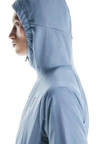 Veste à capuche bleu clair avec une texture lisse, dotée d'une fermeture éclair à l'avant et d'un détail de logo subtil sur l'épaule.