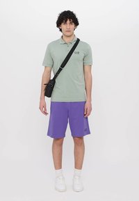 Világoszöld pólóing hímzett logóval, lila sorttal párosítva. A megjelenést fehér sportcipők és egy fekete crossbody táska egészíti ki.