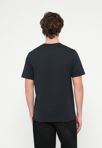 Črna bombažna majica s kratkimi rokavi in okrolim izrezom, prikazana od zadaj, s preprosto zasnovo in enobarvna.