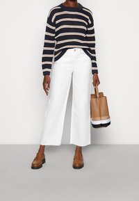 Granatowy i biały sweter w paski, białe dżinsy o szerokich nogawkach z postrzępionym dołem, brązowe loafersy i beżowa torba na ramię z kontrastowym dnem.