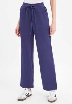 Pantalon ample bleu foncé texturé avec une taille élastique et un cordon, porté avec des baskets blanches à rayures noires.