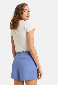 Haut blanc texturé à manches courtes avec des bords en volants, accompagné de shorts bleu clair ornés d'une petite broderie en forme de cœur sur la poche arrière.