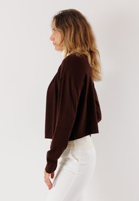 Maglione corto marrone con maniche lunghe, realizzato in tessuto a maglia testurizzata, abbinato a pantaloni bianchi aderenti. Design semplice e vestibilità rilassata.