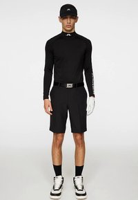 Svart långärmad tröja med logotyp, svarta shorts och vita handskar. Svart keps och svarta strumpor fulländar outfiten, som kompletteras med svartvita sneakers.