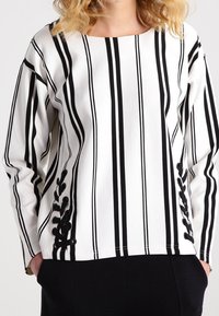 Vit långärmad topp med svarta vertikala ränder och blommiga detaljer. Texturerat tyg, rund halsringning och lös passform med sidodetaljer.