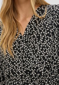 Černé zavinovací šaty s květinovým bílým vzorem, strukturovaná tkanina a výstřih do V. Obsahuje pás na úpravu velikosti v pase.