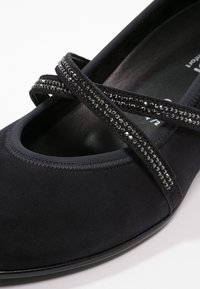 Ballerines en daim noir avec un bout arrondi, des brides croisées ornées de sequins noirs et une doublure intérieure douce. Semelle plate.