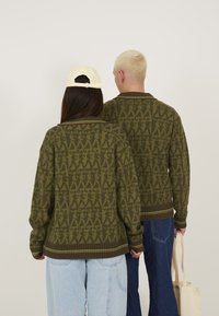 Green knit sweaters with a pattern of abstract shapes. Ribbed cuffs and hem, accented with a thin yellow stripe. Casual, relaxed fit.
