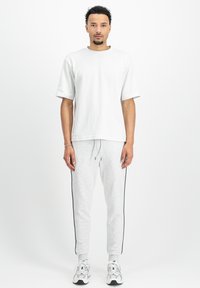 Bela kratka majica s kratkimi rokavi, kombinirana z svetlo sivo trenirko, ki ima črne stranske črte. Čevlji so srebrni in črni športni copati.