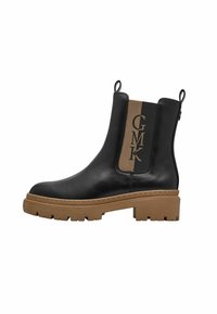 Bottine en cuir noir avec un panneau élastique latéral beige arborant le monogramme "GMK" et une semelle en caoutchouc épaisse pour une meilleure adhérence.