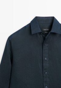 Tmavě námořnicky modrá lněná košile s dlouhým rukávem a klasickým límečkem, s viditelnou značkovou štítkem uvnitř límečku.