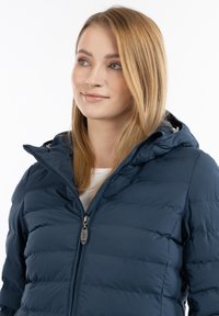 Marinblå pufferjacka med dragkedja, avtagbar huva och kviltad textur. Har hög krage och mjukt tyg.